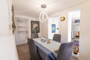 A dining area with a table set for four, a chandelier, and framed artwork on the walls.