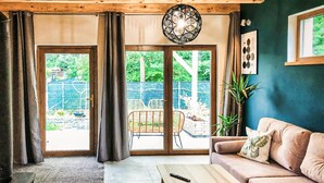 Ein Wohnzimmer mit Sofa, Couchtisch, Pendelleuchte und einer Glasschiebetür zu einem Außenbereich.