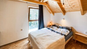 Ein Schlafzimmer mit Holzbalkendecke, einem Bett mit gestreifter Decke, einem Nachttisch mit Lampe und einem Fenster mit Vorhängen.