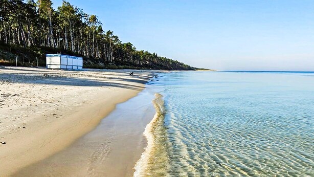 Uma praia com águas cristalinas, areal dourado e um edifício ao fundo.