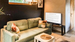 Uma sala de estar com sofá, uma mesa pequena, televisão e luminária.