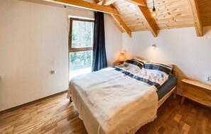 A bedroom with a wooden ceiling, a bed with a striped blanket, a nightstand with a lamp, and a window with a view of trees. - 2 bedroom beautiful home in Kopalino (Kopalino)