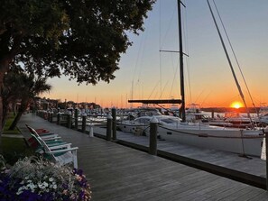 Ein Yachthafen mit vor Anker liegenden Booten, einem hölzernen Steg und einem Sonnenuntergang im Hintergrund.