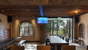 A restaurant interior with a long wooden table, cushioned seating, a television screen, and a brick wall. - Mogan Dreamlohas Sunrise Resort Hotel (Huzhou)