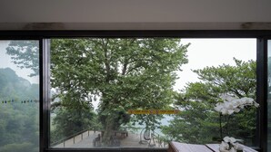A room with a large window overlooking a forested area and a wooden bench with a potted orchid. - Mogan Dreamlohas Sunrise Resort Hotel (Huzhou)