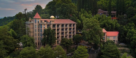 A multi-story hotel with a red roof, surrounded by dense forest.