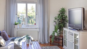 A living room with a sofa, a coffee table, a television on a cabinet, and a window with curtains. - Nice home in Smygehamn with WiFi (Smygehamn)