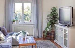 Ein Wohnzimmer mit einer Couch, einem Couchtisch, einem Fernseher auf einem Schrank und einem Fenster mit Vorhängen.