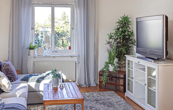 Un salon avec un canapé, une table basse, un téléviseur posé sur un meuble et une fenêtre avec des rideaux.