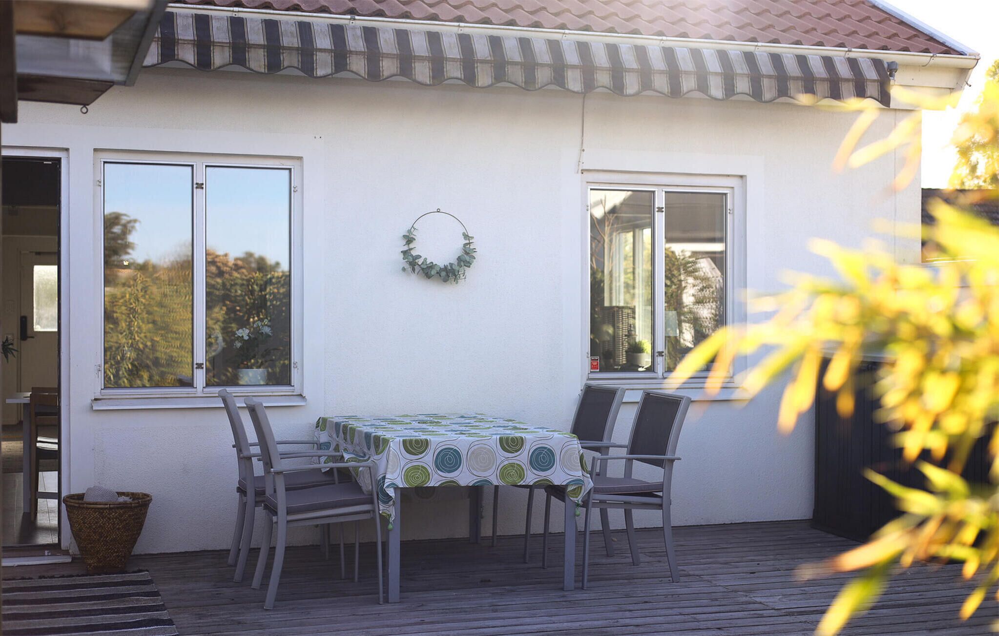 A patio with a table and chairs, a wreath on the wall, and a view of trees through the windows.