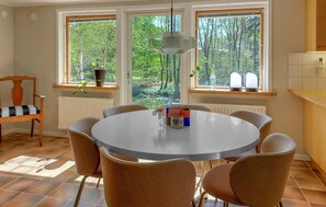 Ein Essbereich mit einem runden Tisch, sechs Stühlen, einer Blumenvase und einem Fenster mit Blick auf Bäume.