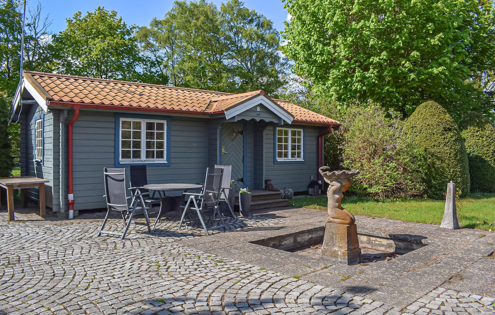 Een huis met pannendak, een veranda met stoelen en een stenen waterput.