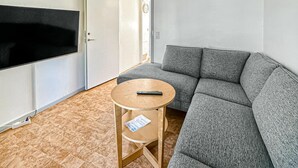 A room with a grey sofa, a small wooden table with a remote control, and a TV mounted on the wall. - Amazing home in Tomelilla with WiFi (Tomelilla)