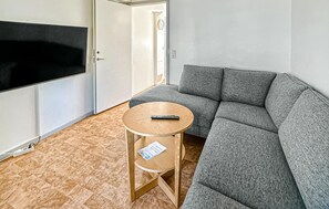 A room with a grey sofa, a small wooden table with a remote control, and a TV mounted on the wall. - Amazing home in Tomelilla with WiFi (Tomelilla)