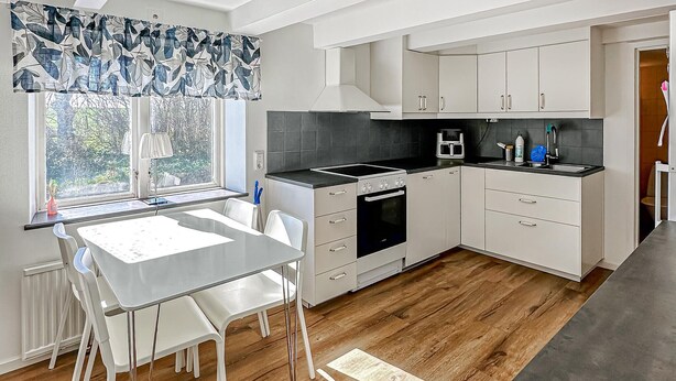 A modern kitchen with white cabinetry, a black countertop, and a dining area with a table and chairs. - Amazing home in Tomelilla with WiFi (Tomelilla)