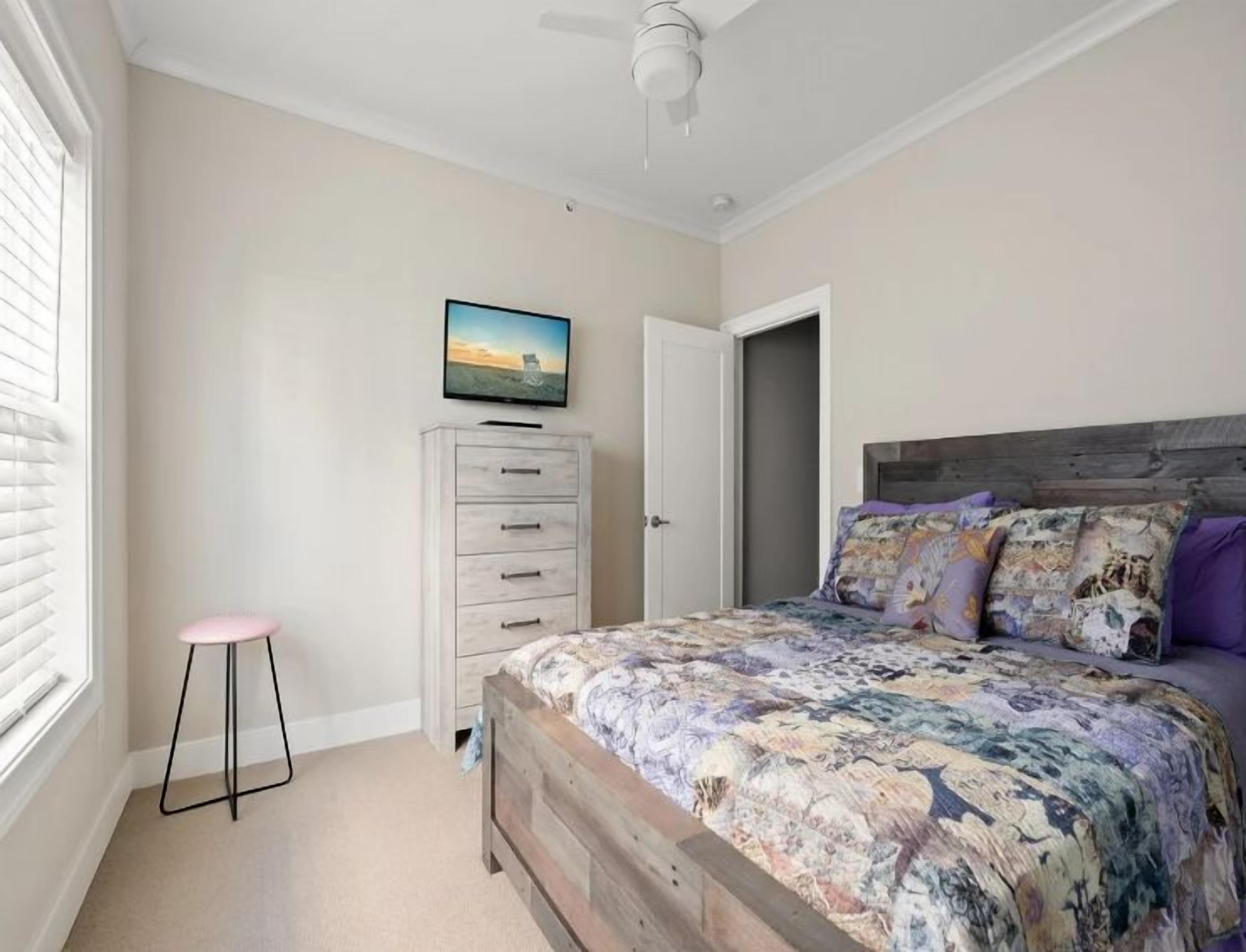A bedroom with a bed, a dresser, a television, and a window.
