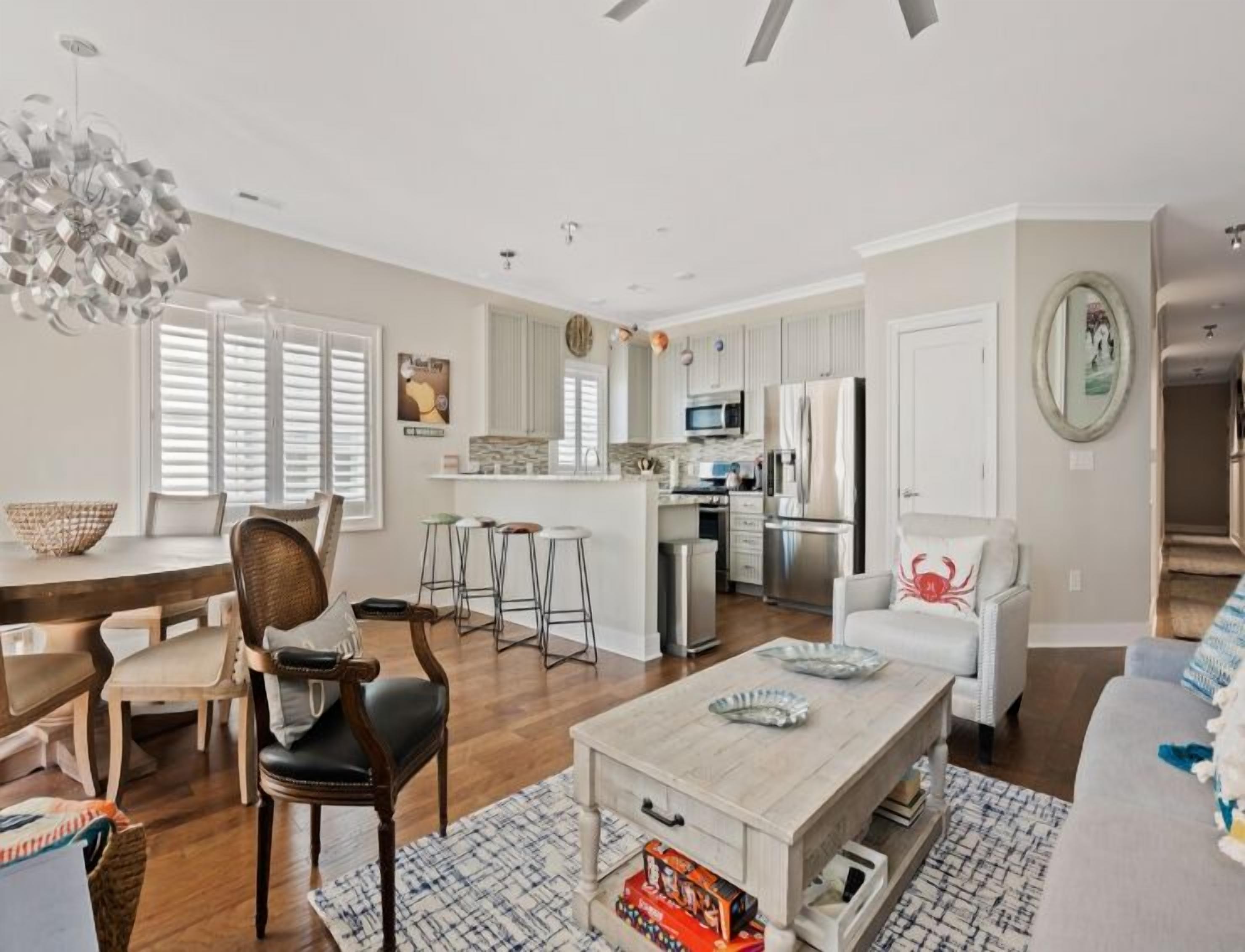 A modern living room with a dining area, kitchen, and a small island. There are multiple seating options including a sofa, chairs, and a bar stool.