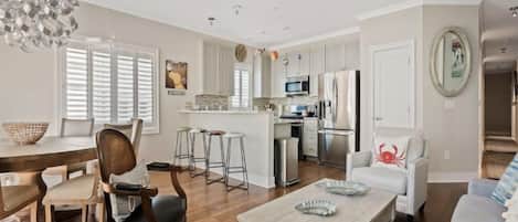 A modern living room with a dining area, kitchen, and a small island. There are multiple seating options including a sofa, chairs, and a bar stool.