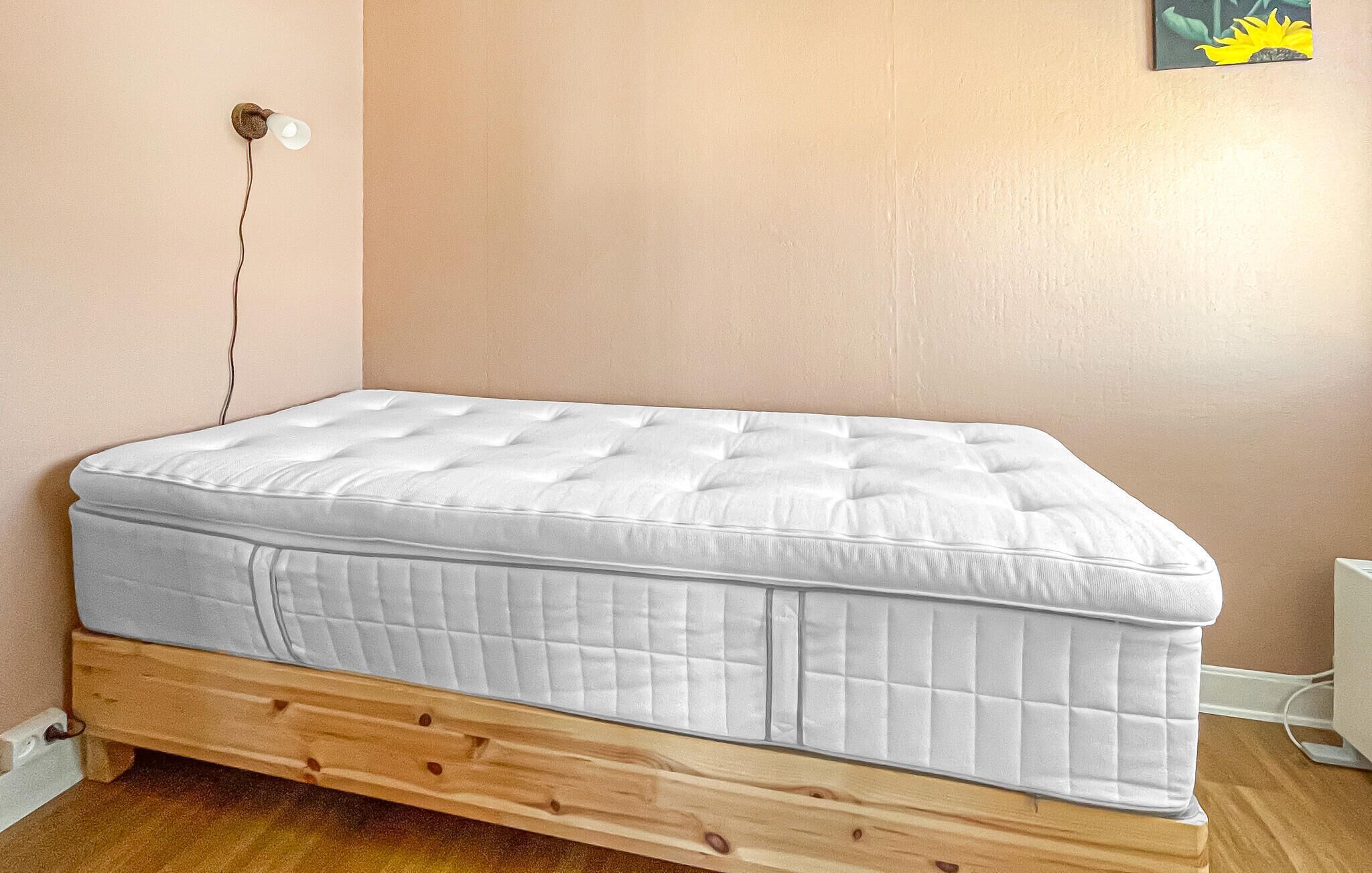 A single-bed room with a wooden frame, a white mattress, and a wall socket.