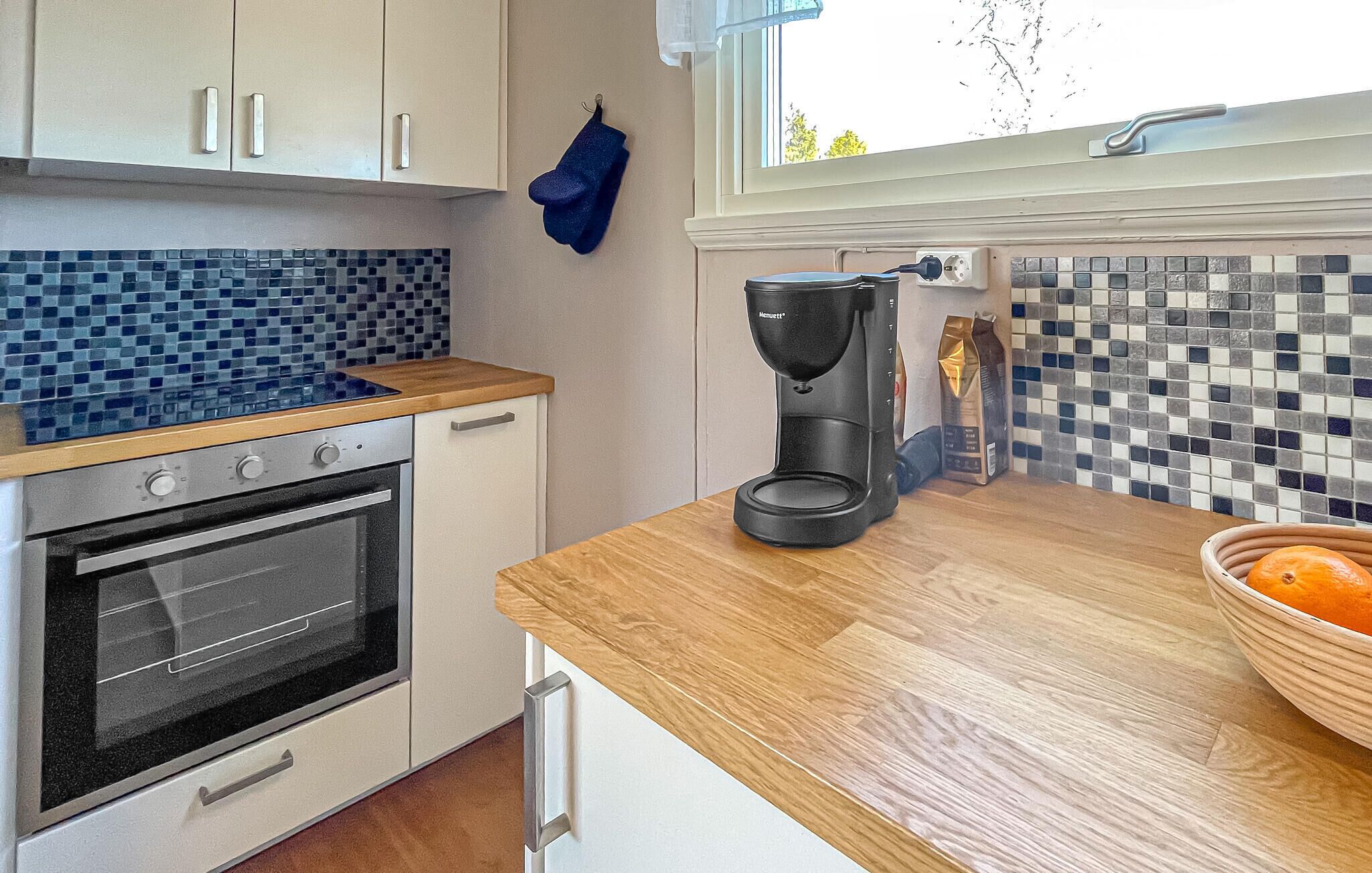 Een keuken met een betegelde spatwand, een koffiezetapparaat, een schaal met fruit en een raam met uitzicht.