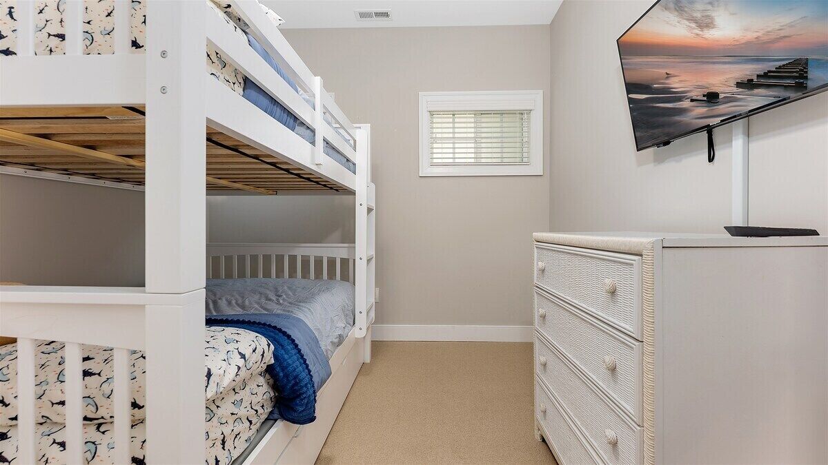 A bedroom with bunk beds, a dresser, a window with blinds, and a wall-mounted TV.