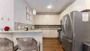 Una cocina moderna con gabinetes blancos, un refrigerador de acero inoxidable y una encimera de granito.