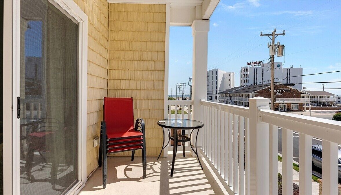 A balcony with a sliding glass door, a red chair, a small round table, and a white railing.