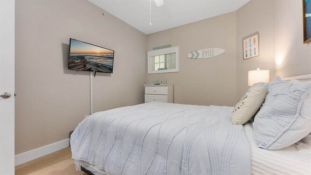 Un dormitorio con una cama, un televisor montado en la pared, un aparador y una ventana con un letrero de temática playera.