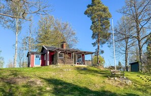 En stuga med en veranda, ett litet förråd och en flaggstång.