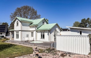 Ein zweistöckiges Haus mit einem grünen Dach, einer Veranda mit Stühlen und einem kleinen Anbau.