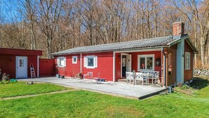 Una casa de madera roja con porche, una puerta y un pequeño jardín.