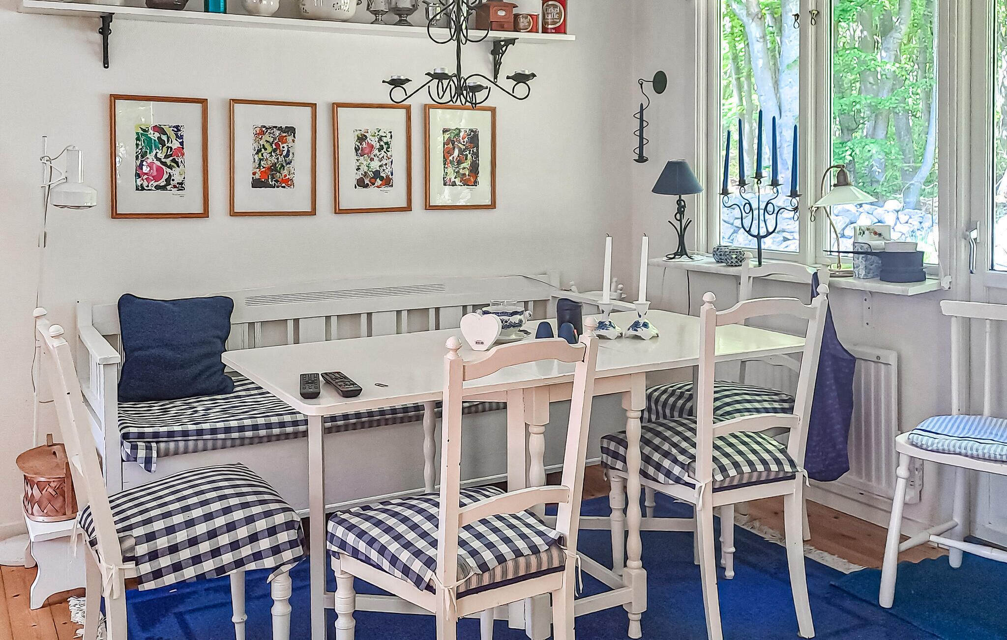 Un coin repas avec une table blanche, quatre chaises dotées de coussins à carreaux, un banc avec un coussin bleu et une fenêtre donnant sur des arbres.