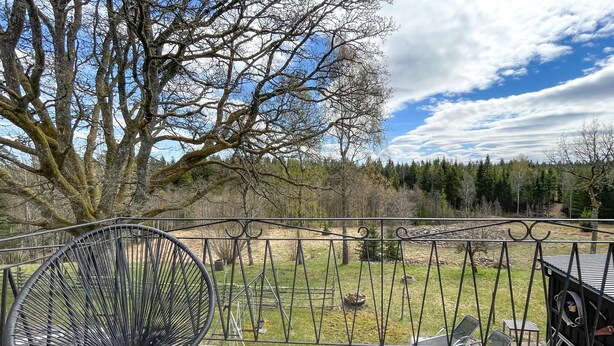 Eine Terrasse mit einem Metallzaun, einem schwarzen Stuhl und Blick auf eine Rasenfläche mit Bäumen.