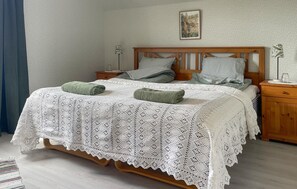 Ein ordentlich bezogenes Bett mit weißer Spitzenhaube, zwei Kissen und einem Holz-Kopfteil.