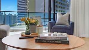 A modern living room with a round wooden coffee table, a vase with flowers, and a stack of books. - Beach Holiday at Oracle Level 7 (Gold Coast)