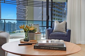 A modern living room with a round wooden coffee table, a vase with flowers, and a stack of books. - Beach Holiday at Oracle Level 7 (Gold Coast)