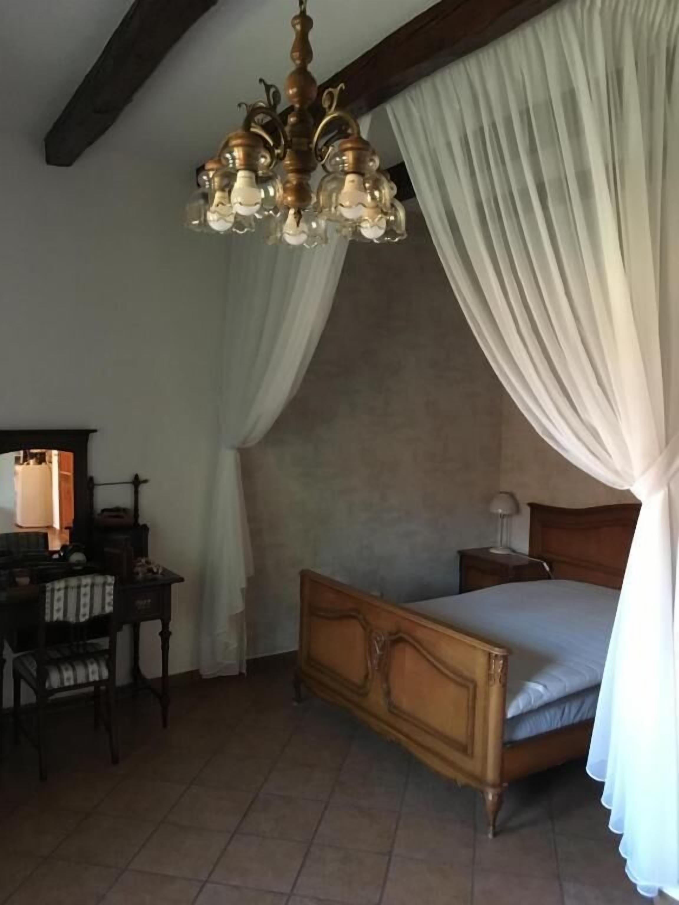 A bedroom with a wooden bed, a nightstand, a desk with a chair, and a chandelier.