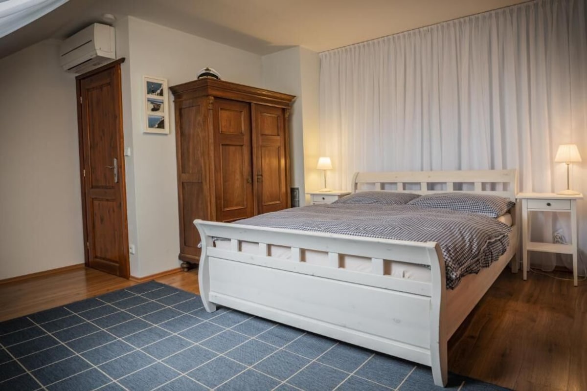 A bedroom with a white bed, wooden wardrobe, and a blue rug.