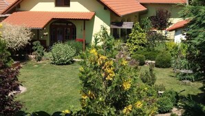 A house with a sloped roof, solar panels, a garden with various plants, and a small pond. - Penzion Primášé (Dolní Věstonice)