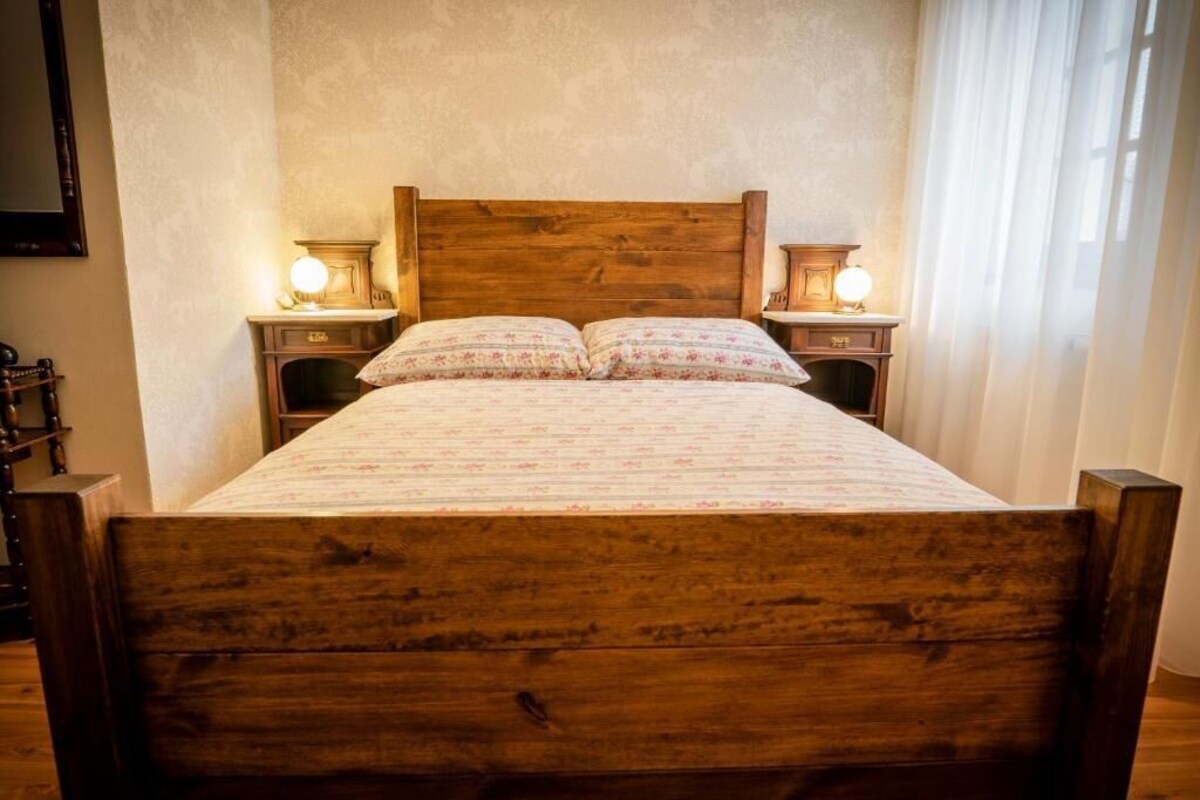 A wooden bed with a floral bedspread, two bedside lamps, and a mirror on the wall.