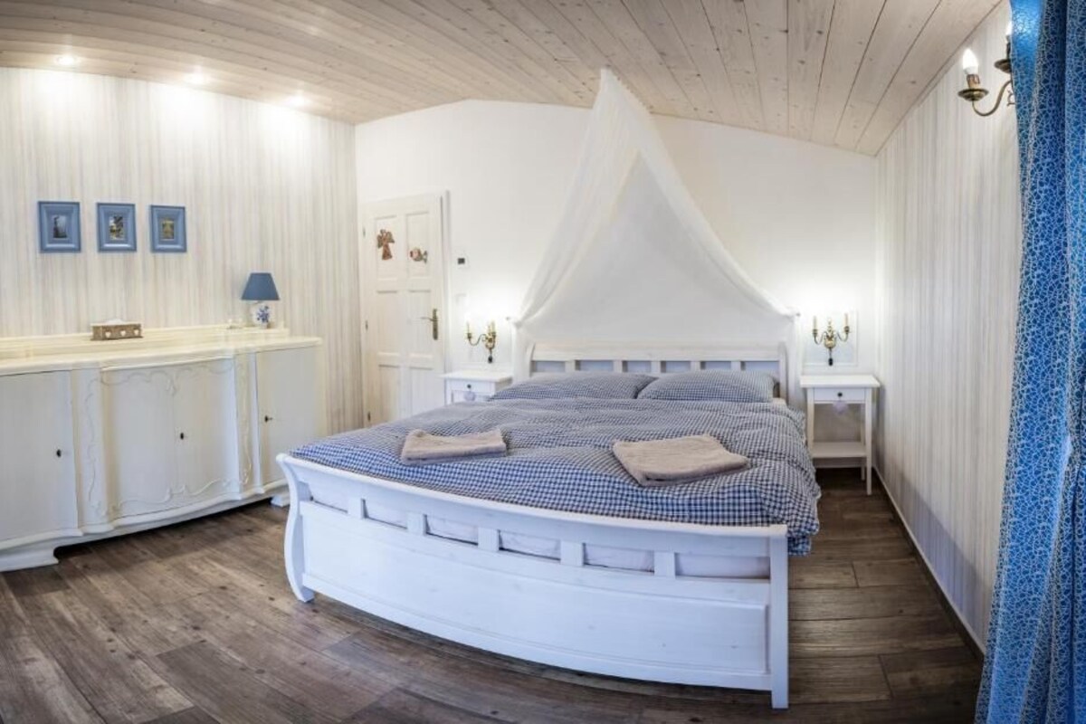 A bedroom with a white canopy bed, bedside tables, a dresser, and framed pictures on the wall.