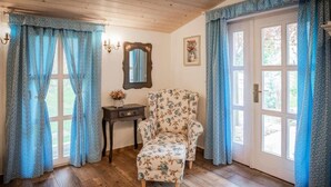 A room with wooden flooring, a floral armchair, a small table with a vase, and blue curtains. - Penzion Primášé (Dolní Věstonice)