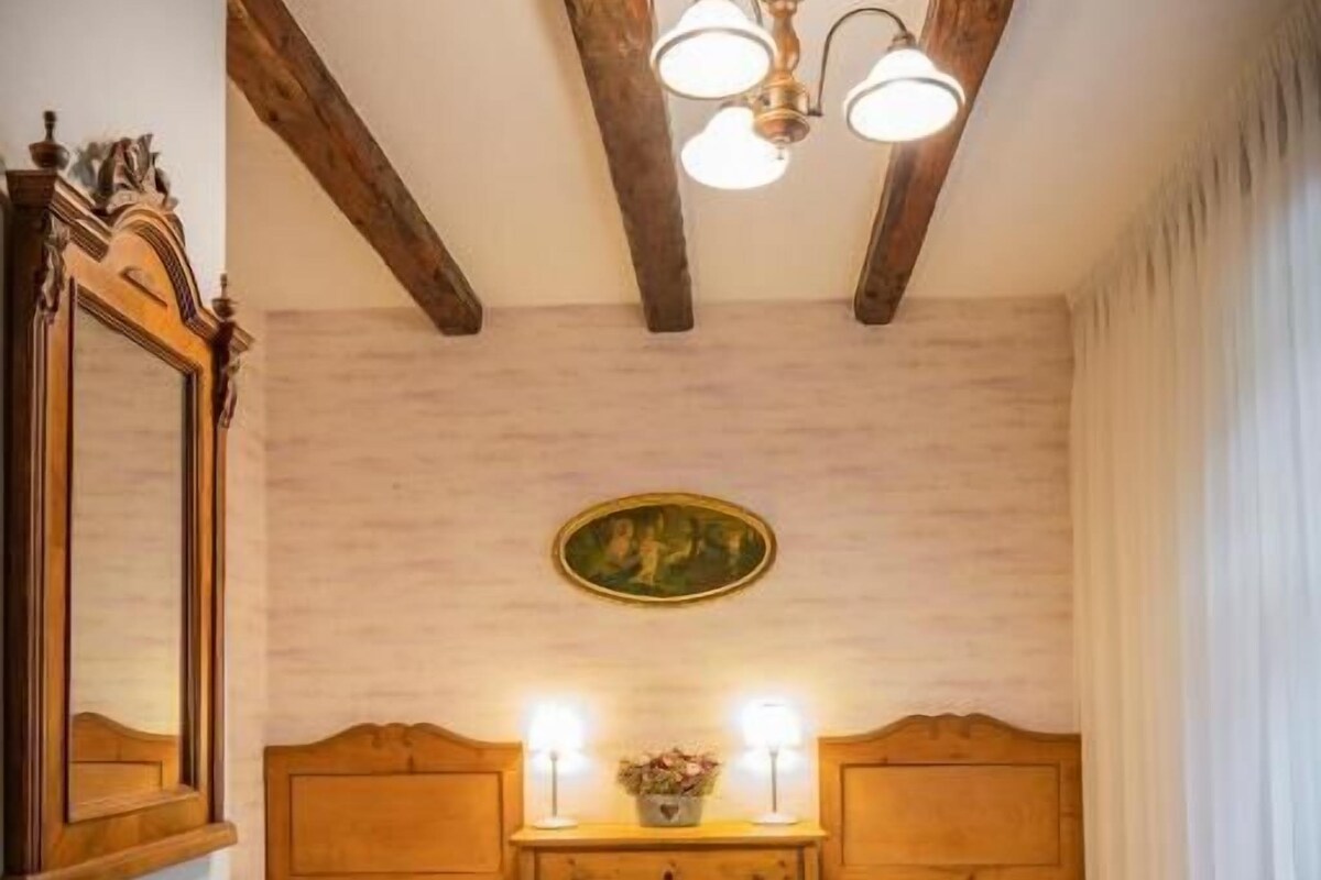 A room with two wooden beds, a wooden dresser, a chandelier, and a mirror.