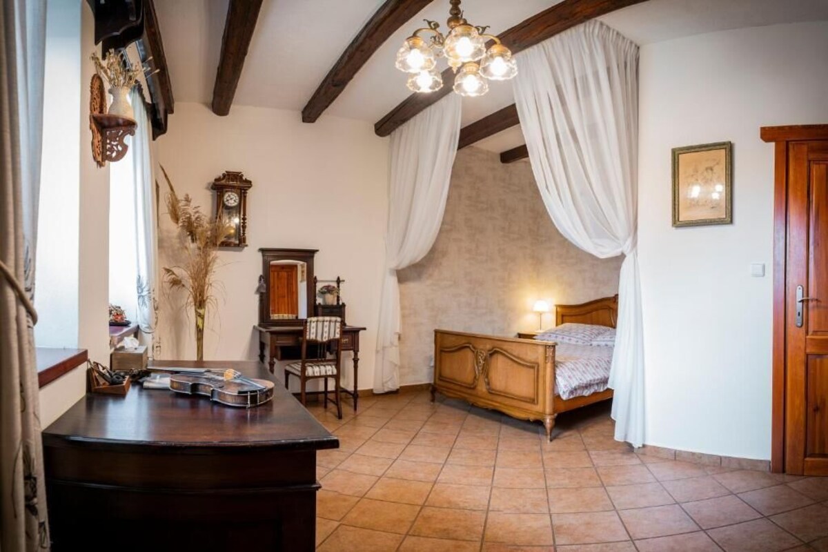 A bedroom with a wooden bed, a nightstand, a dresser, a mirror, a clock, and a chandelier.
