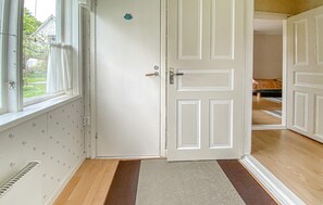 Ein Zimmer mit weißer Tür, einem fensterbehangenen Fenster, einer Wand mit Muster und einem Holzboden.