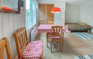 Ein gemütliches Zimmer mit einem karierten Tisch, Holzstühlen, einem Bett und einem Fenster mit Vorhängen.