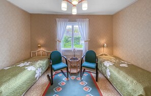 Ein Zimmer mit zwei Einzelbetten, einem kleinen Tisch, zwei Stühlen, einem Fenster mit Vorhängen und zwei Wandleuchten.