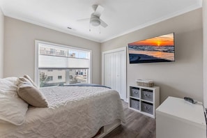 A bedroom with a bed, a ceiling fan, a window with a view, a TV on the wall, and a white cabinet. - Residence 201S at The Sandcastle Condominiums (Wildwood Crest)