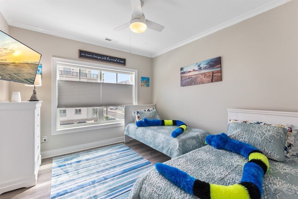 A bedroom with two beds, a window with blinds, a ceiling fan, and a view of a building outside.