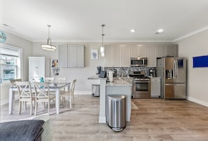 A modern kitchen with white cabinets, stainless steel appliances, and a dining area with white chairs. - Residence 201S at The Sandcastle Condominiums (Wildwood Crest)